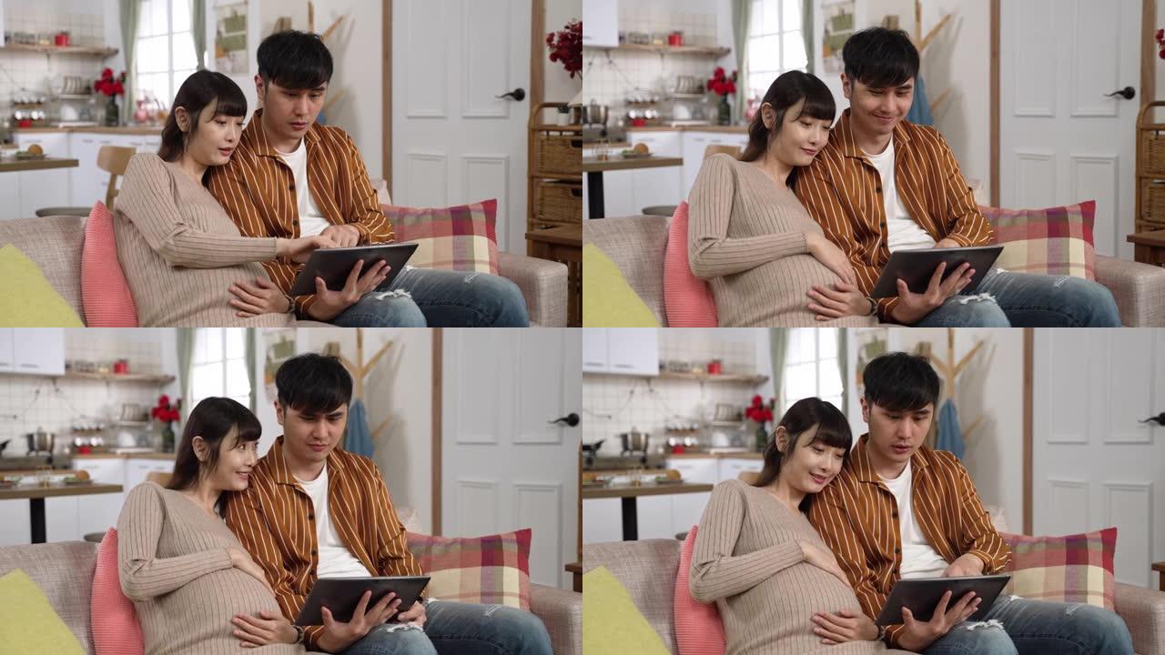 快乐的亚洲孕妇夫妇在家里客厅沙发上的电子垫一起网上购物婴儿用品