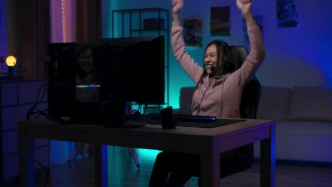 快乐的玩家女孩坐在电脑前戴着耳机，专业的游戏设备，女人赢了回合，过关了，胜利用手跳舞