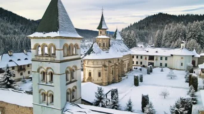罗马尼亚冬季普特纳修道院的空中无人机视图。内院有步行的游客，光秃秃的树木，雪，周围的山丘