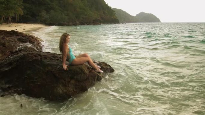 女人冷静放松休息在海礁石上，暴风雨多云的海洋。穿着泳衣的女人束腰外衣。概念休息热带户外旅游