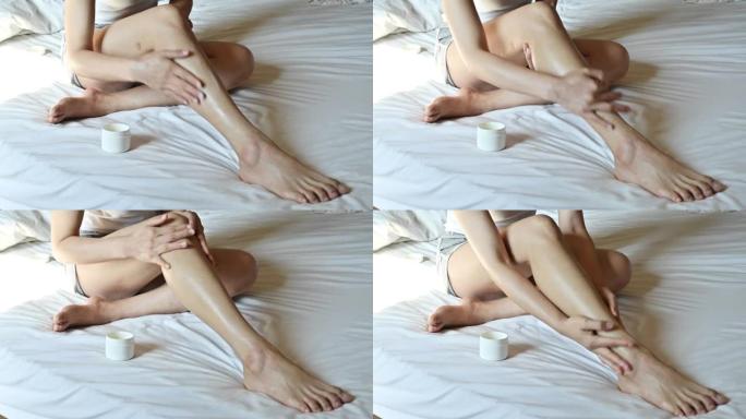 年轻的亚洲女性坐在床上，同时在腿上涂抹防晒霜，以反射太阳的紫外线 (UV) 辐射，从而有助于防止晒伤