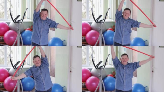一个患有唐氏综合症的快乐残疾人对着镜头微笑正在进行体育锻炼，我将一根体操棒举到顶部。