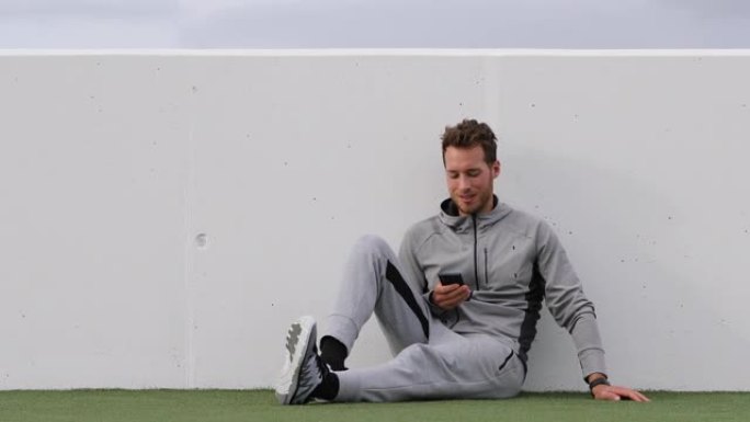 健身男子在户外休息时使用手机应用程序放松。积极的生活方式年轻人拿着智能手机观看在线视频或发短信短信。
