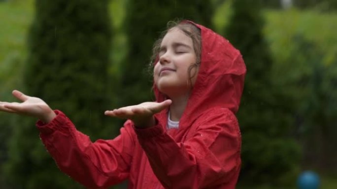 儿童在下雨的夏日在户外玩耍。快乐的小女孩在雨中微笑。孩子热爱自然，幸福自由。玩水滴雨的孩子。穿着红色