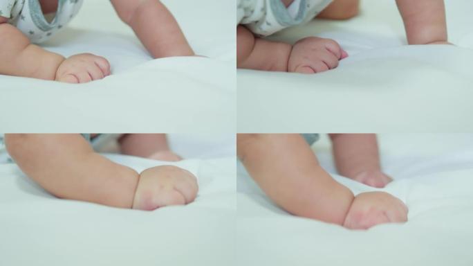 特写可爱的婴儿新生的小手伸到爬行或躺在白色床上玩耍。幸福的家庭，天真的小新婴儿可爱的新生活和为人父母