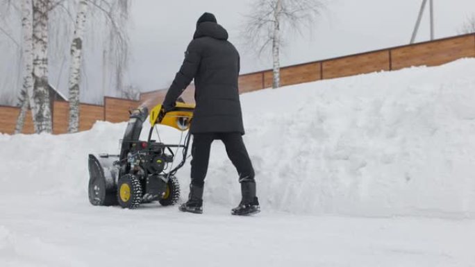 男子在院子里用机械扫雪机除雪。雪粉。慢动作