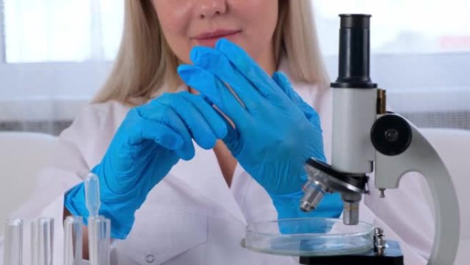 女科学家实验室助理完成了在显微镜下研究试管中微生物的工作，并脱下了防护手套。一个女人在显微镜下的实验