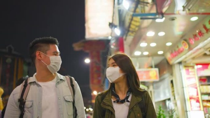 亚洲迷人的夫妇晚上在城市里度蜜月旅行。年轻的新婚男女背包客游客戴上口罩，以防止Covid19，一起度