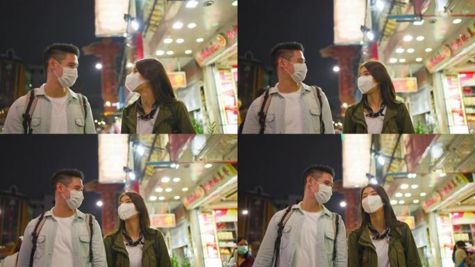 亚洲迷人的夫妇晚上在城市里度蜜月旅行。年轻的新婚男女背包客游客戴上口罩，以防止Covid19，一起度