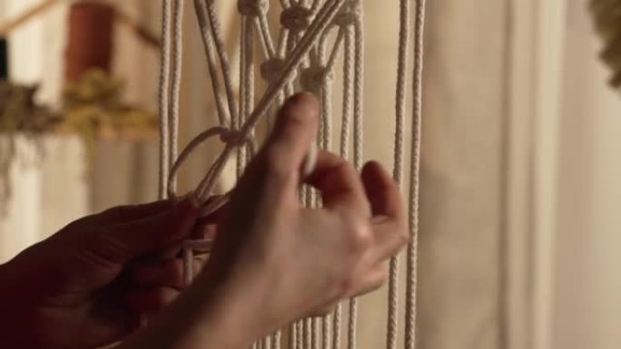女人在自己的家庭车间的棍子上编织图案的花边。女性双手打结，形成一条线。手工制作的概念。妇女在针线活过