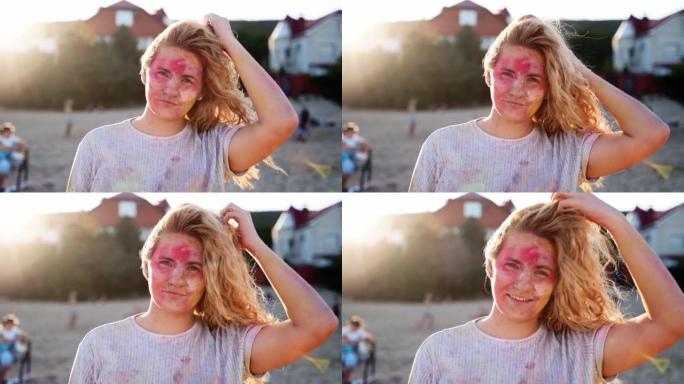 年轻女子沾满了彩色的粉末，长长的波浪状金发看着站在海滩上的相机。户外印度教节日派对上的女孩。封锁结束