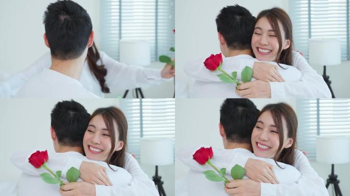 亚洲年轻人惊喜并将玫瑰花送给美丽的女友。迷人的浪漫新人男女坐在床上，一起庆祝周年纪念日和情人节
