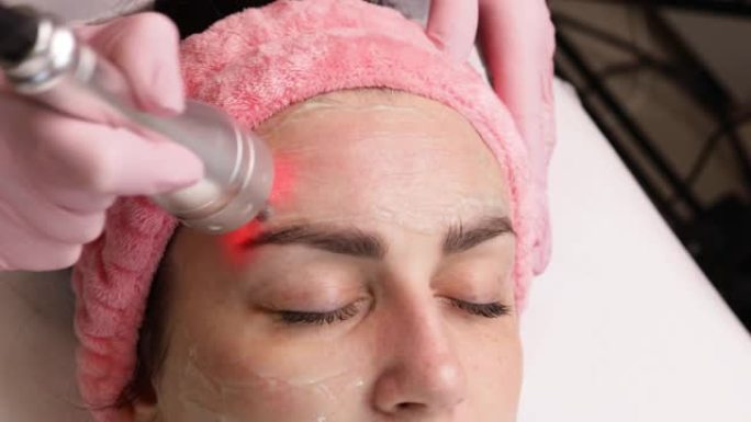 美容师制作生物发光射频提升程序。恢复皮肤活力，防止衰老，女人得到刺激美容面部护理。现代诊所的硬件美容