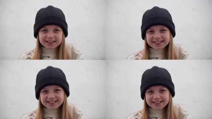 开朗的积极向上的学龄女孩，戴着白色背景上的温暖帽子。她看着镜头时微笑着。