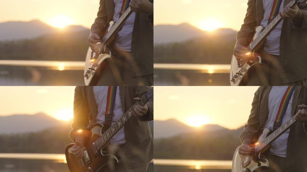 英俊的卷发亚洲男子在日落时在湖边弹吉他和唱歌度假。