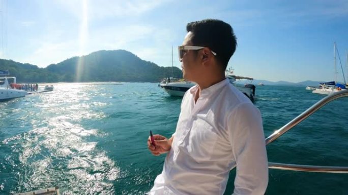 肖像自信的亚洲年轻人站在游艇上向前看和微笑
