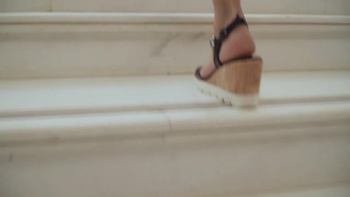 穿着凉鞋的女人的脚爬楼梯。坡跟凉鞋