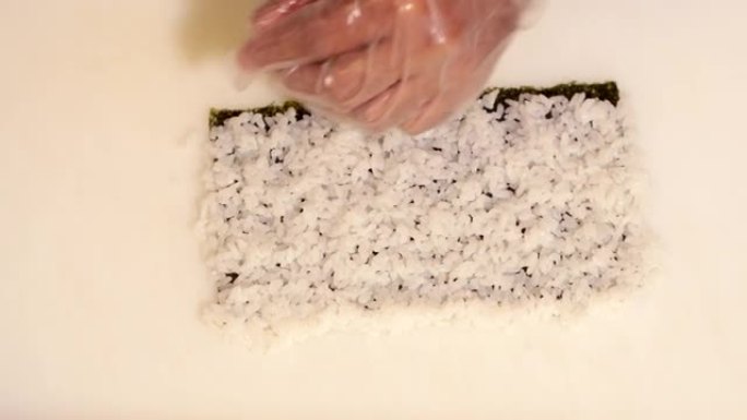 厨房里的厨师在紫菜上撒米饭，在竹席上做寿司卷