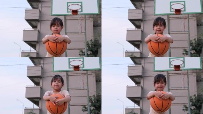 开朗可爱的女孩拿着篮球在户外篮球操场上看着相机。