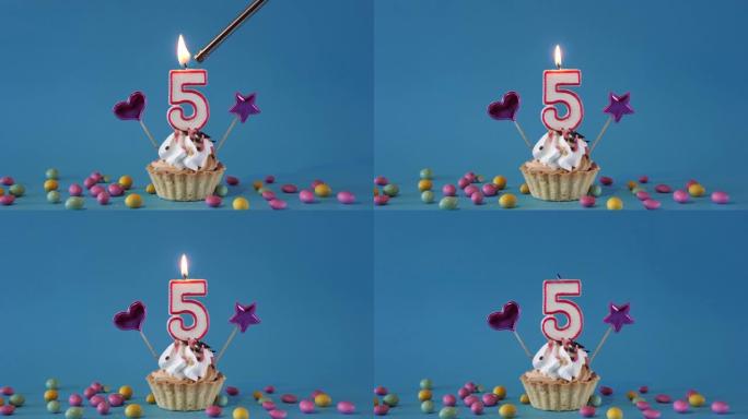 祝5岁的孩子生日快乐，带蜡烛的生日蛋糕和蓝色背景上的生日装饰品。点燃并熄灭纸杯蛋糕上的节日蜡烛