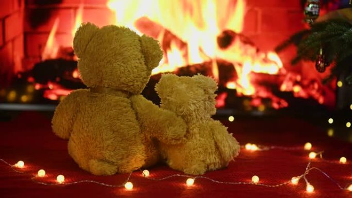 两个可爱的泰迪熊互相拥抱，坐在针织的红色格子上，背景是灯泡的花环和燃烧的壁炉