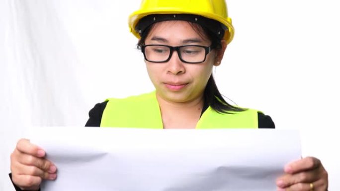 戴着头盔的女建筑师在工作室的白色背景上看着施工计划。美女土木工程师看蓝图和检查草稿地图。