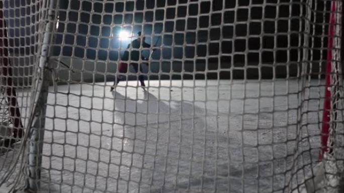 曲棍球前锋网背后的观点，他用棍子击中冰球并进球。慢动作冰球飞入网中的特写镜头。带有聚光灯和烟雾的黑暗