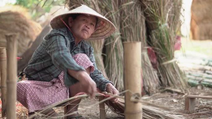 亚洲生活老奶奶在户外工作。老太太老人严重生活在泰国农村的农村。编织材料草屋顶毛边竹制。