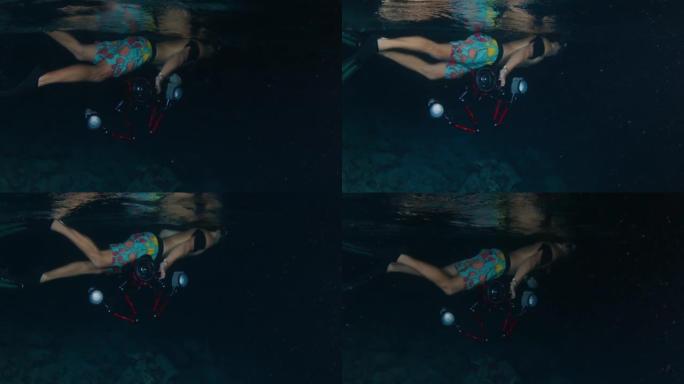 夜间水下摄影。男性水下摄影师的肖像在热带海洋中夜间穿着装备游泳