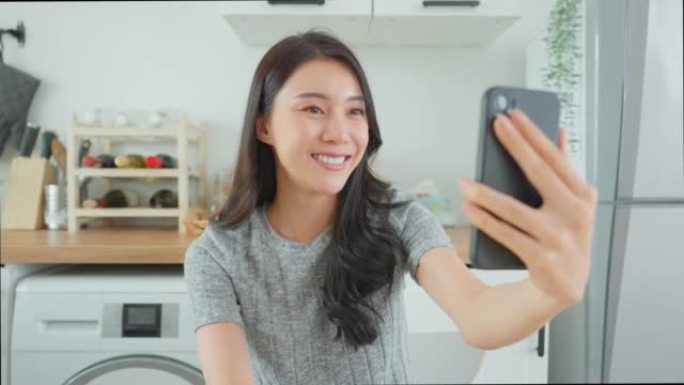 亚洲迷人的女人在卧室里使用手机视频通话。穿着睡衣的亚洲美女博客作者拿着智能手机，在家里聊天在线虚拟电