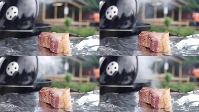 野餐派对上吸烟烧烤吸烟者的背景下，铝箔上有多汁的肉牛排和脆皮。周末在烧烤网格上烤肉的过程，户外烤肉概
