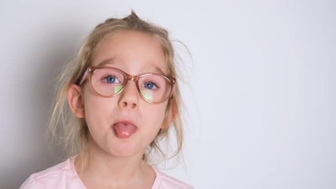 戴着眼镜和粉红色t恤的小女孩沉迷，玩得开心，露出舌头，对着镜头做鬼脸。4k分辨率视频横幅，带复制空间
