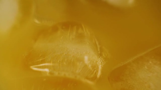 冰块的特写旋转并漂浮在木制桌子上的水器中的新鲜橙汁中