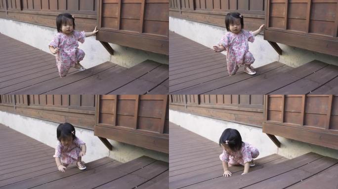 穿着和服的天真的日本小女孩刚学会走路，在屋外的木楼梯上迈出了她的第一步，却失去了平衡