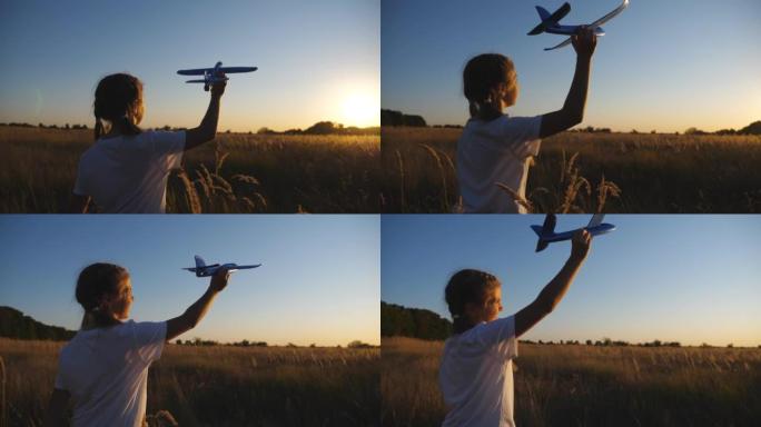 可爱的女孩子玩玩具飞机沿着草地散步。日落时分，无忧无虑的小孩坐飞机在草地上。享受自由的微笑的小女孩。