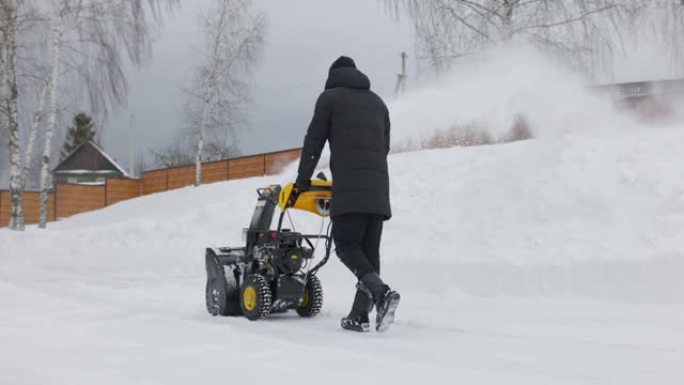 一名男子在慢动作的降雪中，用吹雪机在院子里扫雪