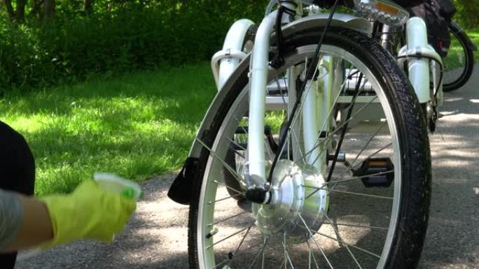 戴着黄色手套的骑自行车的人在夏天喷洒清洁外面的电动自行车电动轮。骑手照顾带电机的运动电动自行车车轮。