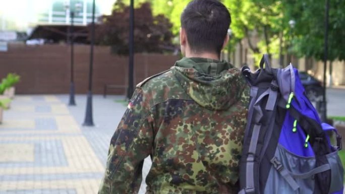 一名身穿迷彩服的士兵，肩上背着一个大袋子。从后面看。缓慢的莫