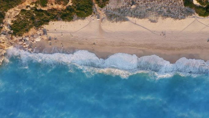 希腊莱夫卡达米洛斯海滩。金色的沙子和荧光的绿松石海浪的俯视图。无法识别的人在日落时欣赏夏天的场景
