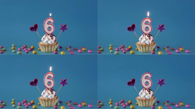 祝6岁的孩子生日快乐，带蜡烛的生日蛋糕和蓝色背景上的生日装饰品。点燃并熄灭纸杯蛋糕上的节日蜡烛