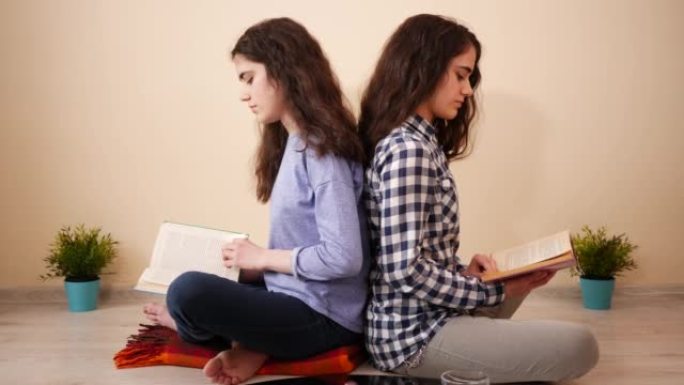 两个十几岁的女孩在家里的双胞胎姐妹坐在一起阅读带有真实纸页的书