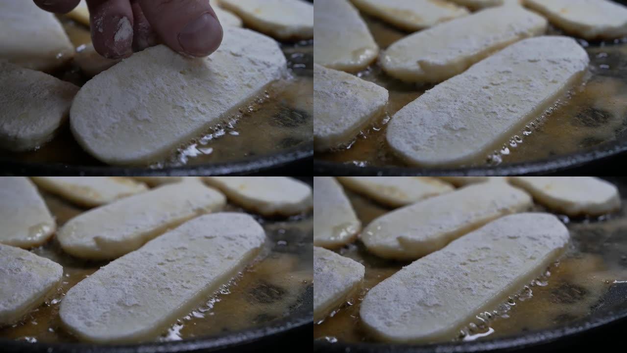 厨师的手指将奶酪块放入煎锅中的热油中