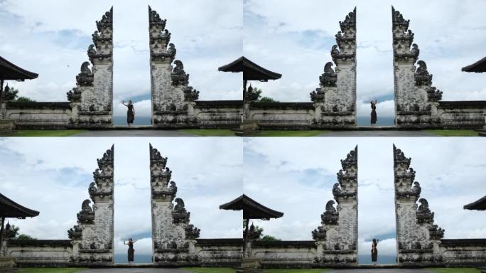 在多云的天气中拥抱著名的巴厘岛大门，女性游客在美妙的风景中自拍。大门后面是美丽的云，通往天堂的大门