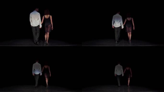 男女舞厅舞者夫妇走进舞台黑暗，步态缓慢，手牵手看着对方，穿着黑白舞蹈服装，后视。结束舞蹈表演概念