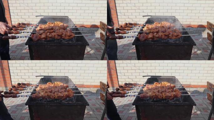 在烤架上慢动作煮多汁，酥脆的烤肉串。男性手在烤架上煎炸串的特写