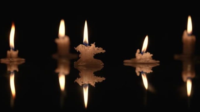 在黑色背景上燃烧蜡烛，烛光反射在光滑的表面上。石蜡蜡烛的存根在黑暗中闪烁。纪念、哀悼或庆祝的背景或插