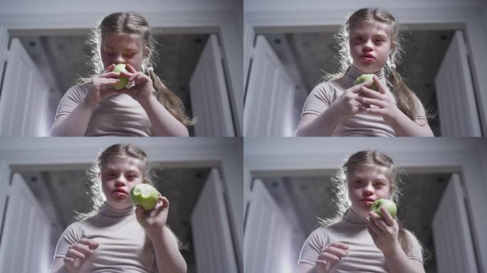 一个患有唐氏综合症的女孩正在咬一个青苹果。健康食品。残疾人在家。残疾生活