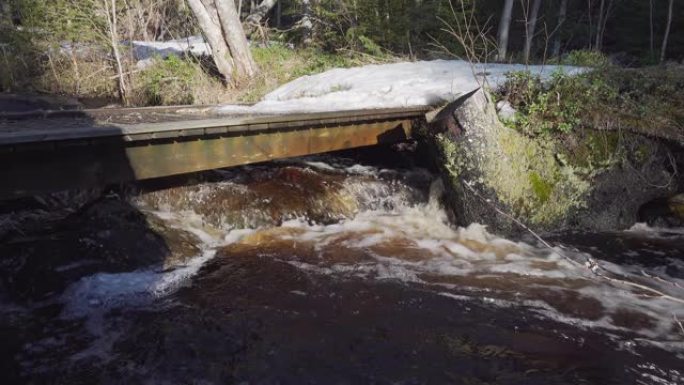 森林小溪上非常小的木制平桥，下面有很多水流。靠近自来水的森林里融化的雪。瑞典、欧洲。流水原声