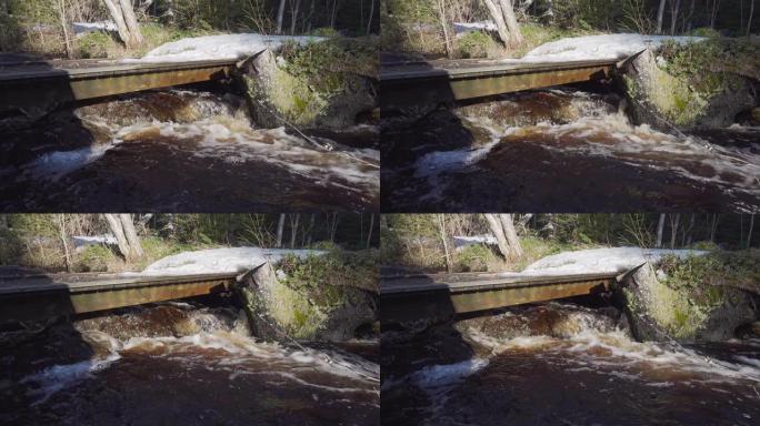 森林小溪上非常小的木制平桥，下面有很多水流。靠近自来水的森林里融化的雪。瑞典、欧洲。流水原声