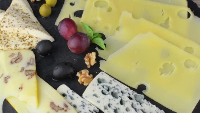 奶酪拼盘搭配各种奶酪，葡萄，黑色背景上的坚果。意大利奶酪和水果拼盘在石板旋转背景上。